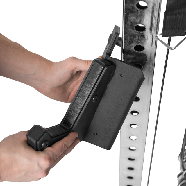 Close-up of hands adjusting a black safety spotter arm onto the Bells of Steel Functional Trainer Cable Tower with adjustable height holes, contrasting against the clean white background.
