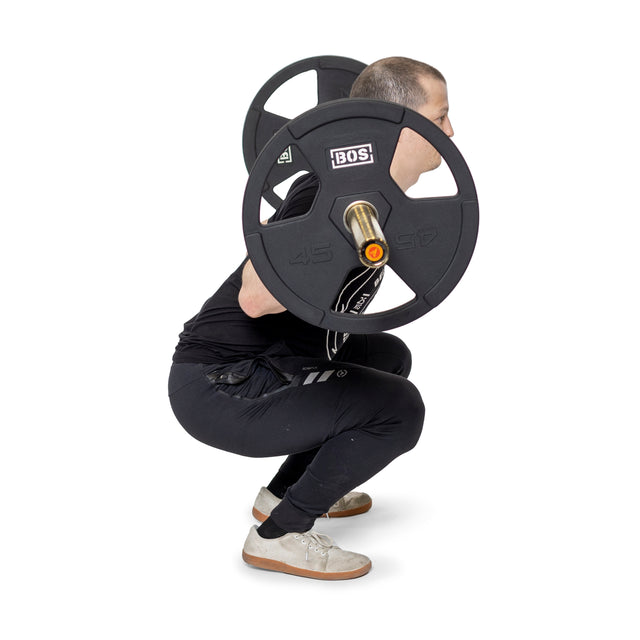 A person in black attire squats with a weighted barbell featuring Bells of Steel Rubber Coated Iron Weight Plate Sets for durability, knees bent and back straight against a white background.