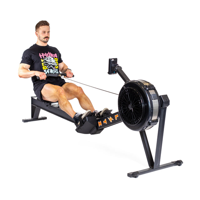 A person in a black T-shirt is demonstrating the rowing motion on a Blitz Air Rower by Bells of Steel, positioned on a white background. The machine exemplifies low-impact cardio and offers a full-body workout.
