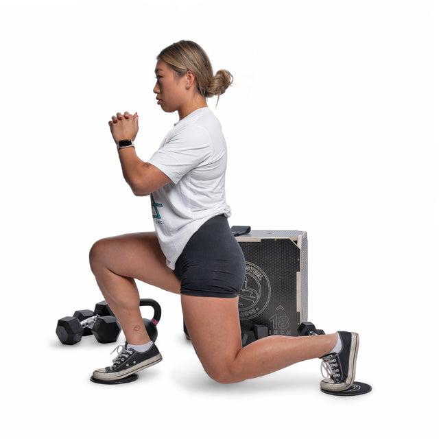 A woman in a white t-shirt and black shorts lunges with a slider, with Bells of Steel Strength Circuit Starter Kits in the background, demonstrating an effective home workout on a white backdrop.
