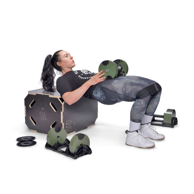 A woman hip thrusts with dumbbells and a bench, her upper back resting on the bench, feet flat. Bells of Steel Strength Circuit Starter Kits sit nearby—an ideal setup for home workouts.
