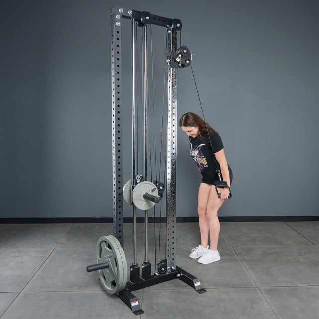 A woman in athletic wear uses the Bells of Steel Fat Bar – Single D Handle on a cable machine for triceps in a gym with gray walls, elbows at her sides and looking down to boost grip strength.