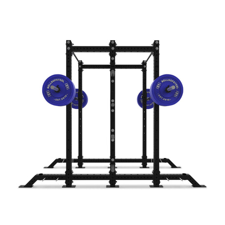 The Bells of Steel Hydra 2-Sided Rack is a sturdy black metal power rack with two blue barbells, featuring a rectangular frame and multiple adjustment holes—ideal for modular home gyms and strength training.