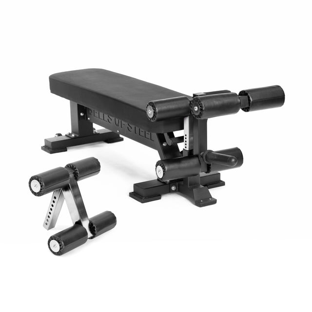 The Bells of Steel Hero Heavy-Duty Weight Bench in black features padded rollers for leg support and comes with a matching compact leg attachment, all shown on a white background.