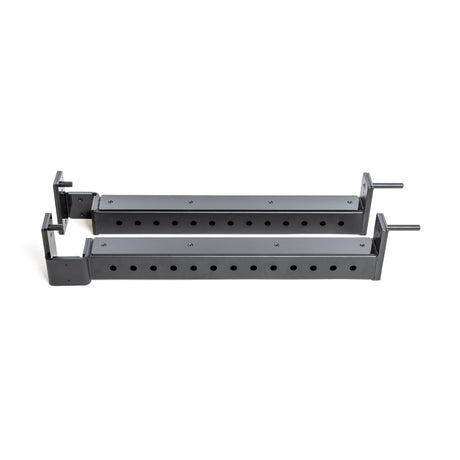 Two black metal Flip-Down Safeties by Bells of Steel, featuring multiple holes for height adjustment, are positioned parallel on a white background, ensuring training safety when used with a power rack.