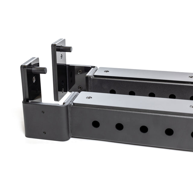 Two black metal Bells of Steel Flip-Down Safeties with multiple holes and angled hooks, designed for mounting or supporting heavy equipment on a power rack. The brackets are positioned parallel on a white background.