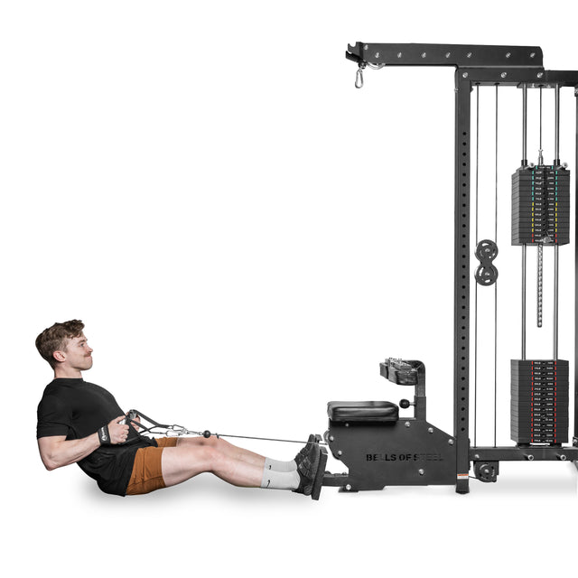 A man wearing a black t-shirt and brown shorts performs a seated cable row exercise using the upgraded machine. Seated upright on a padded bench, he grips the Aluminum Handles Pair with Bearings from Bells of Steel USA, focusing intensely on his workout.