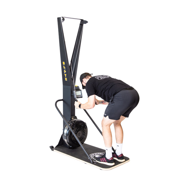 Wearing athletic gear, a man uses the Bells of Steel Blitz Ski Trainer, pulling its handles down for a focused, full-body workout that mimics the motion of cross-country skiing.