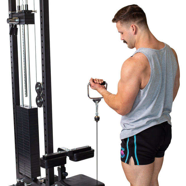 A man in a gray tank top and black shorts performs a tricep pushdown on a cable machine using the Bells of Steel Single D Handle Cable Attachment, gripping the handle with both hands while standing sideways to the camera.