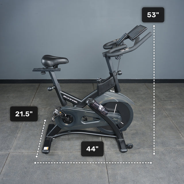 A Bells of Steel Blitz Indoor Cycling Bike with adjustable features is placed on a tiled floor against a gray wall, measuring 21.5" wide, 44" long, and 53" tall.