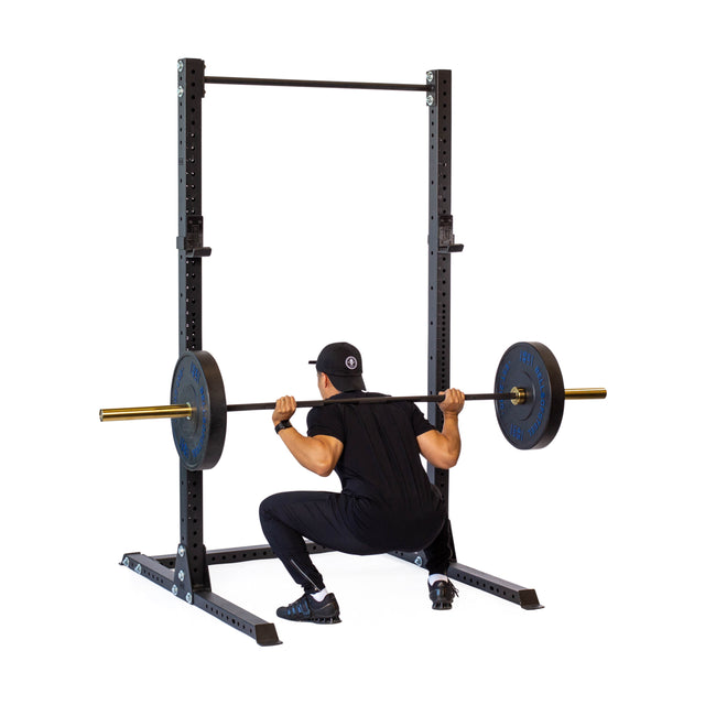 Dressed in black athletic wear, a person performs a barbell squat using the Bells of Steel Hydra Squat Stand - Prebuilt (3" x 3", ⅝" Holes) against a white background—ideal for any home gym.