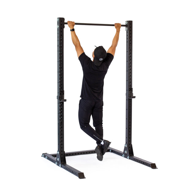 A person in black workout gear and a cap does a pull-up on the Bells of Steel Hydra Squat Stand - Prebuilt (3" x 3", ⅝" Holes) against a plain white background, ideal for any home gym.