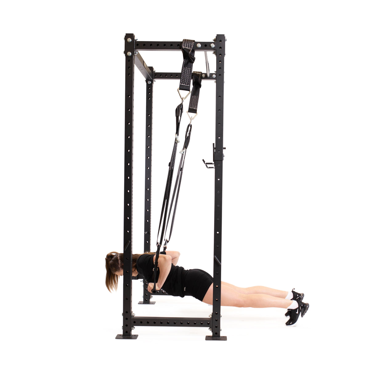Using the Bells of Steel Suspension Spotter Straps And Bodyweight System, a person highlights core and upper body strength in a home gym by performing an inverted row on gymnastic rings attached to a tall metal frame, parallel to the floor and wearing a black outfit with sneakers.
