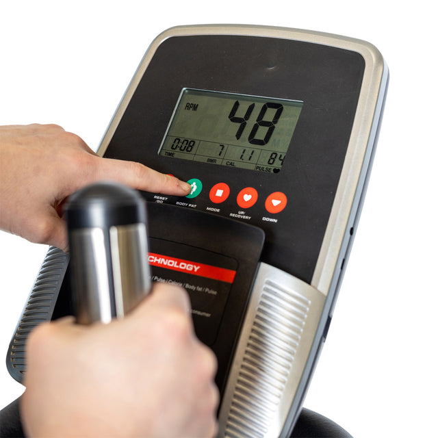 Close-up of a hand pressing a green button on the Bells of Steel Blitz Stepper’s control panel, with a digital display showing workout info and another hand gripping the handle for effective low-impact cardio.