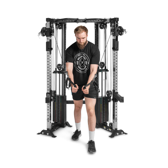 A man in a black T-shirt and shorts performs a cable crossover on the Bells of Steel Functional Trainer Cable Tower with adjustable weights, set in a gym environment.