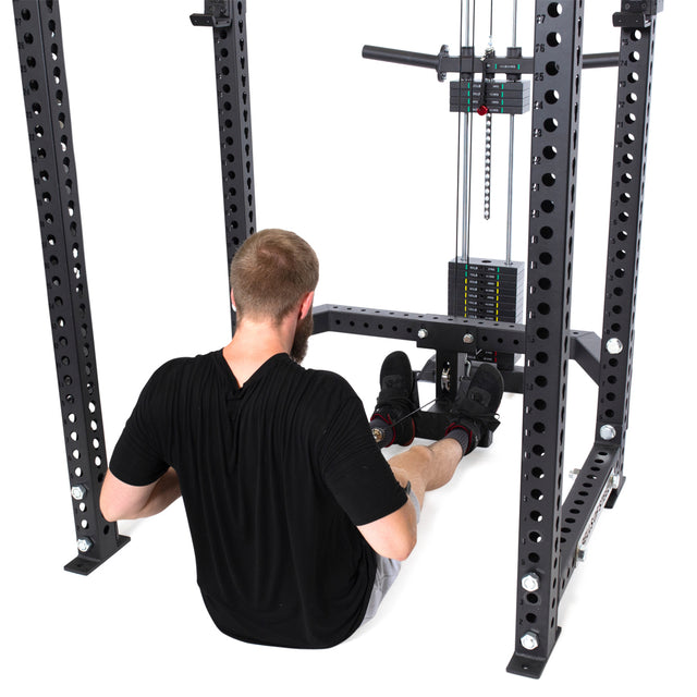 Using the Lat Pulldown & Low Row Rack Attachment - Hydra & Manticore by Bells of Steel, a person performs seated cable rows. They sit gripping the handle connected to the low row attachment with a weight stack behind them on a black steel frame with multiple holes.