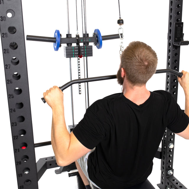 Wearing a black shirt, a man expertly uses the Bells of Steel Lat Pulldown & Low Row Rack Attachment for Hydra & Manticore with a wide grip bar. He adeptly handles the weight stacks and adjustable pulleys within the metal frame, displaying his cable exercise expertise.