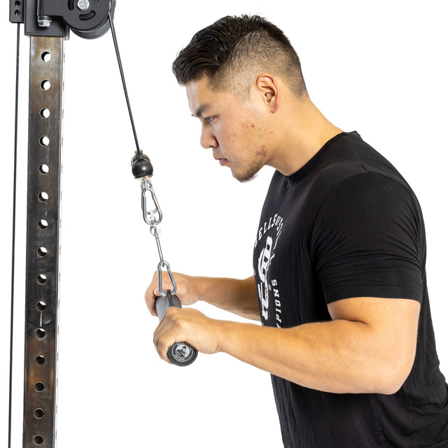 A man in a black T-shirt performs a tricep pushdown with the Bells of Steel Fat Bar - Straight Handle Bar, gripping the bar with both hands and keeping elbows close to his body against a white background.