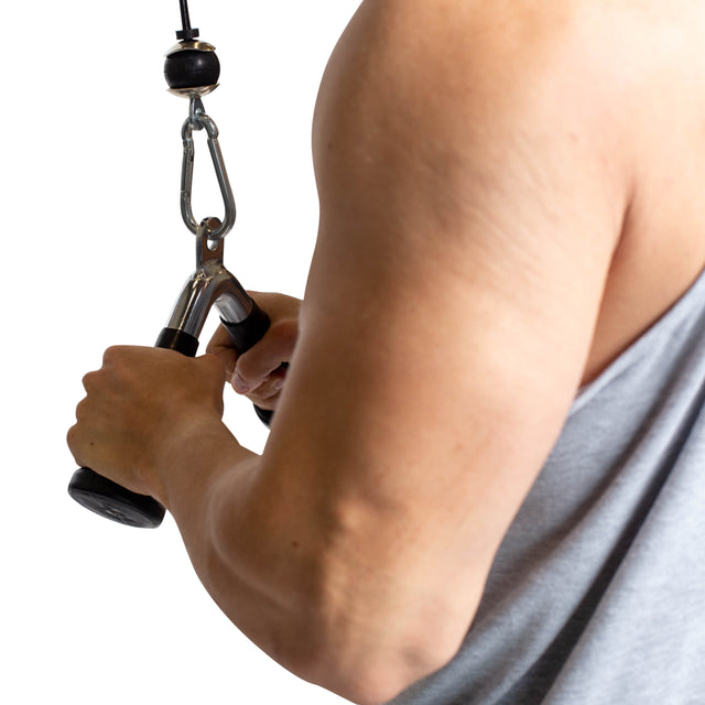 A person uses the Bells of Steel Tricep Pressdown With Ergo Handgrips on a cable machine, performing the exercise in a gray sleeveless shirt against a white background.