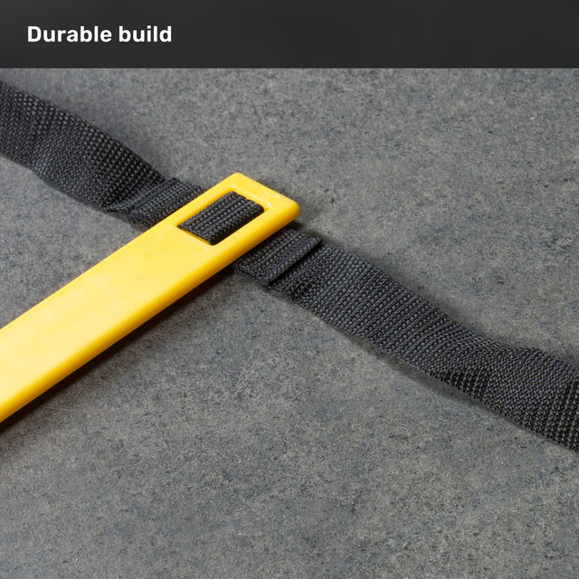 A yellow plastic bar attached to a black woven strap rests on a gray surface, with the caption “Durable build” displayed at the top. This piece is part of the Agility Ladder and Leg Cord Bundle from Bells of Steel USA, designed for agility training and to enhance any speed and agility kit.