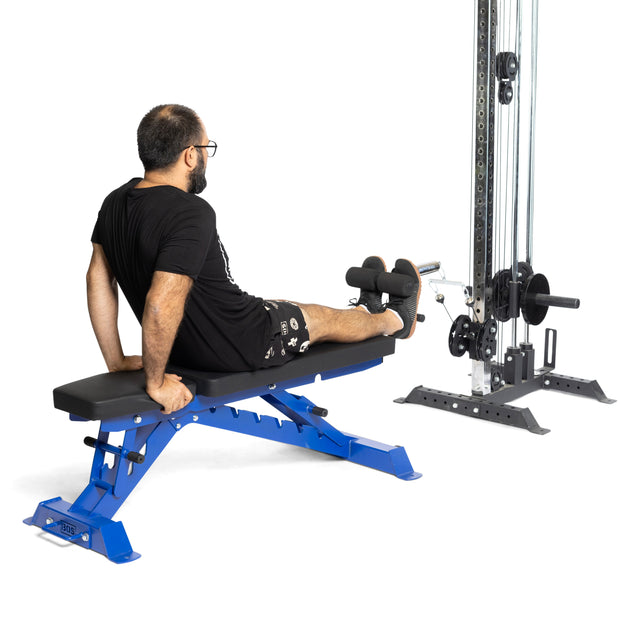 A man uses the Bells of Steel Tibialis Trainer Bar with Olympic plates, focusing on leg exercise and knee injury prevention, while sitting on a blue bench and facing away from the camera.