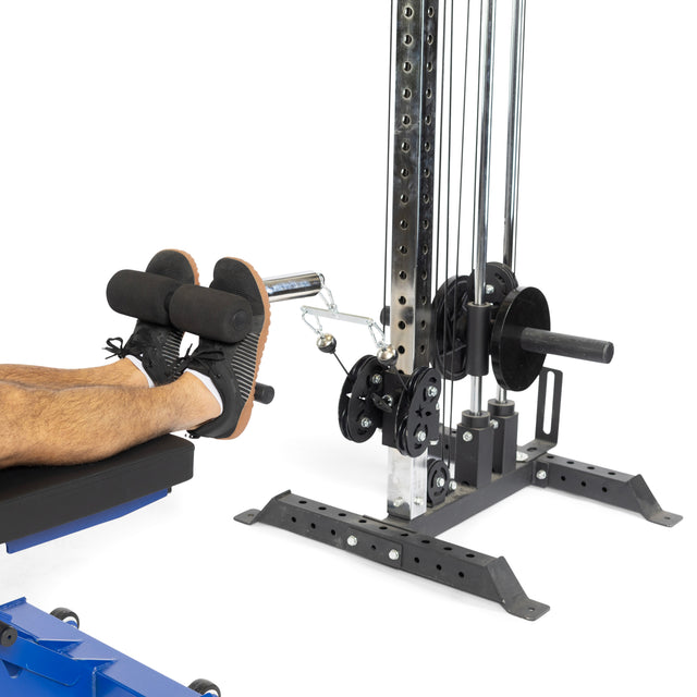 A person uses the Bells of Steel Tibialis Trainer Bar, hooking their feet under padded rollers for leg exercises with Olympic weight plates, supporting strength training and knee injury prevention.