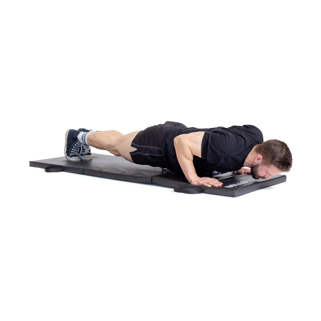 A man in athletic wear does a push-up with elbows bent and chest close to the mat, using the Bells of Steel Trifold Mat for a stable, non-slip surface.