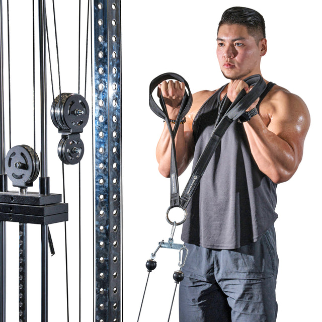 A man in athletic apparel performs a cable curl using the Bells of Steel RocIT Tricep Strap, gripping the attachment with both hands as weight plates and pulleys are visible on the fitness machine.