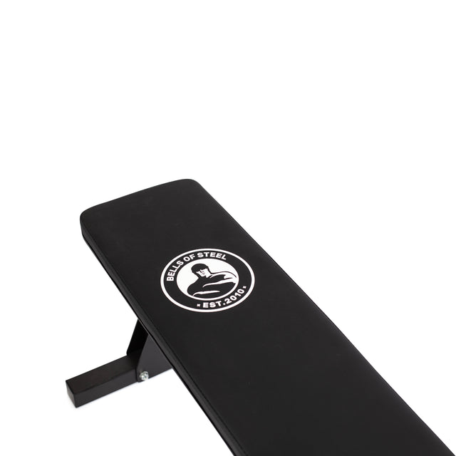 The Bells of Steel Flat Utility Bench, shown in black with the "Bells of Steel Est. 2010" logo on the padded surface, offers a sturdy, budget-friendly design and supports up to 661 lb.