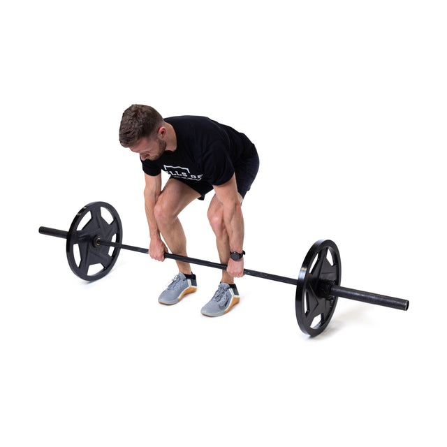 A man in a black shirt and shorts bends to lift a barbell with Black Mighty Grip Olympic Weight Plates by Bells of Steel, featuring precision grip handles. He sports gray sneakers and a watch, set against a plain white background.