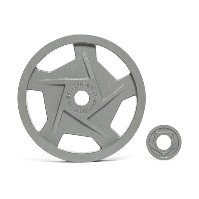 A large Gray Mighty Grip Olympic weight plate with an ergonomic, star-shaped cutout sits next to a smaller one; both have a durable hammertone powder coat and feature "Bells of Steel." The large plate is on the left, and the smaller is on the right.