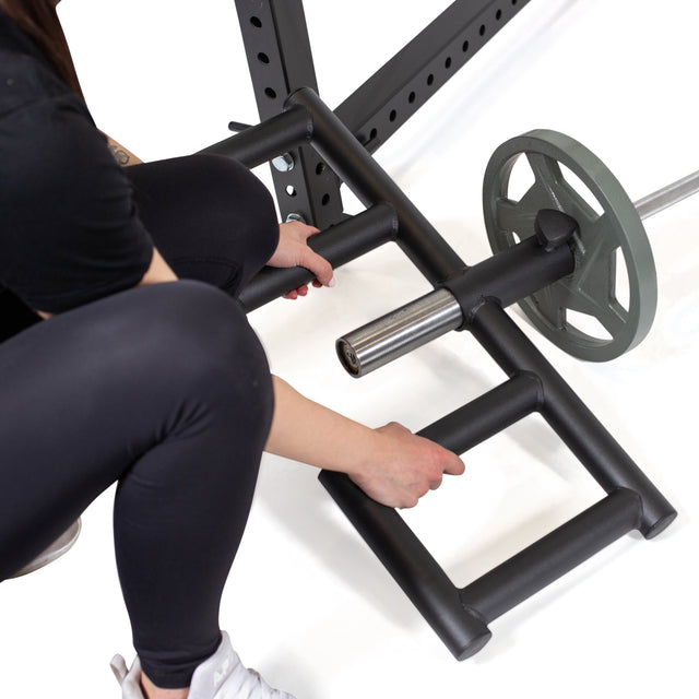 Wearing black athletic wear, a person grips the Bells of Steel Viking Press Attachment on an Olympic bar with plates, preparing for a landmine row.