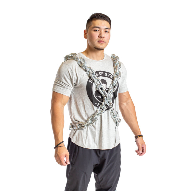 A man stands confidently wearing the Bells of Steel Chain Weight Vest, with weighted chains draped over his shoulders and chest, demonstrating strength training against a plain white background.