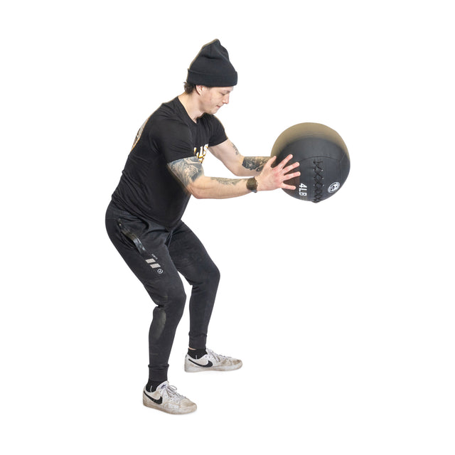 Against a white backdrop, an individual in black attire holds a Triple Stitched Medicine Ball by Bells of Steel. Their focused expression and slightly bent stance radiate high fitness levels as they gear up for an intense workout session.