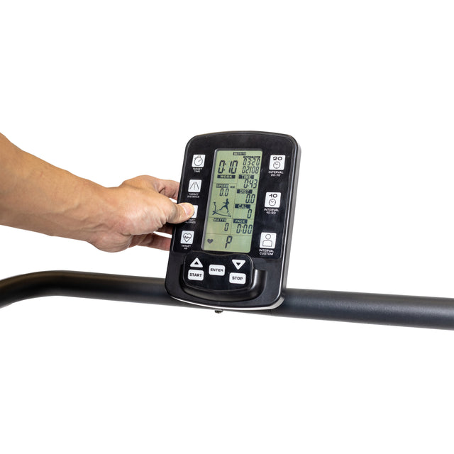 A user's hand presses a button on the Wooden Residential Manual Treadmill by Bells of Steel, showing settings like start, stop, and workout levels on the control panel. The compact design is mounted on a sleek black handlebar.