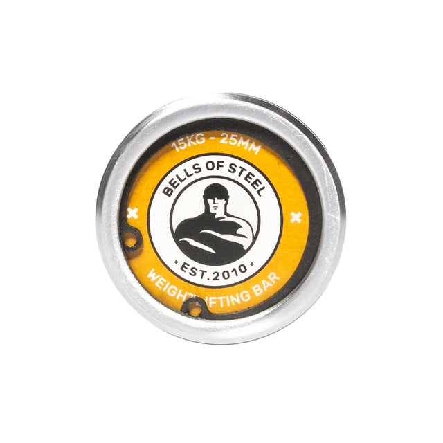 Close-up of the end cap on the Bells of Steel Oly Lifting Needle Bearing Bar - Women's, showing the brand logo, a muscular figure, and "15KG - 25MM Weightlifting Bar EST. 2010" on a yellow and silver background.