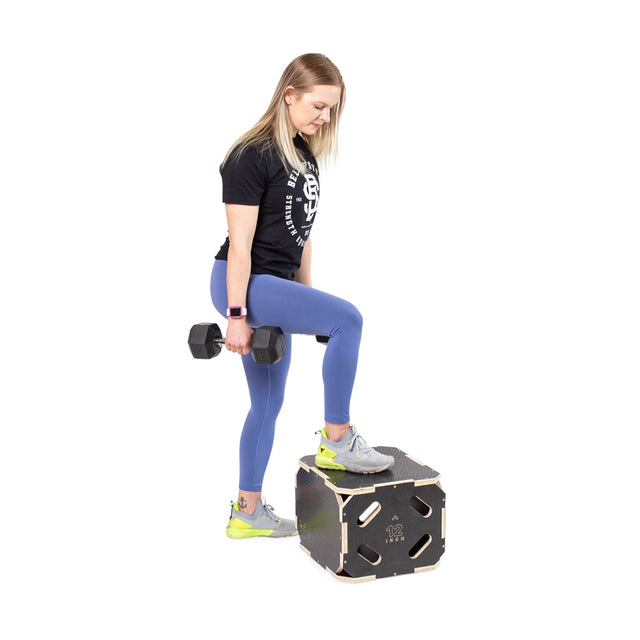 A woman in athletic wear steps onto a Bells of Steel 3 in 1 Anti-Slip Wood Plyo Box with her left foot, holding a dumbbell, showcasing non-slip gym equipment against a white background.
