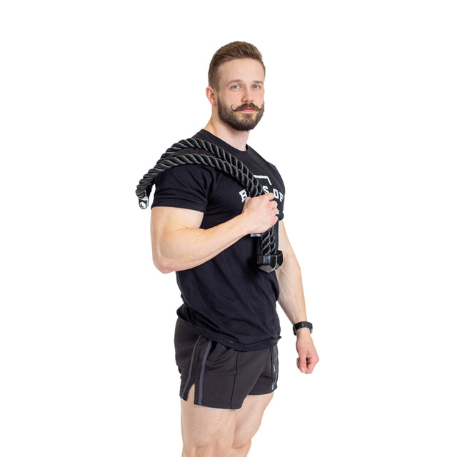 A bearded man against a white background wears a black T-shirt and shorts, holding the Bells of Steel Extra Long Tricep Rope Extension (137cm) over his shoulder—ideal for tricep pushdowns—and looks at the camera.