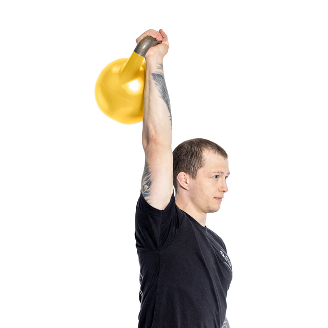 A person in a black t-shirt lifts a yellow, Bells of Steel Adjustable Competition Kettlebell overhead with one arm. Intricate tattoos adorn their forearm against the plain white background.