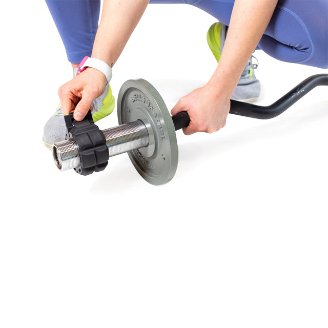 A person in blue leggings and yellow-green sneakers is securing a weight plate with black Bells of Steel Barbell Zip Clips on a barbell against a white background.