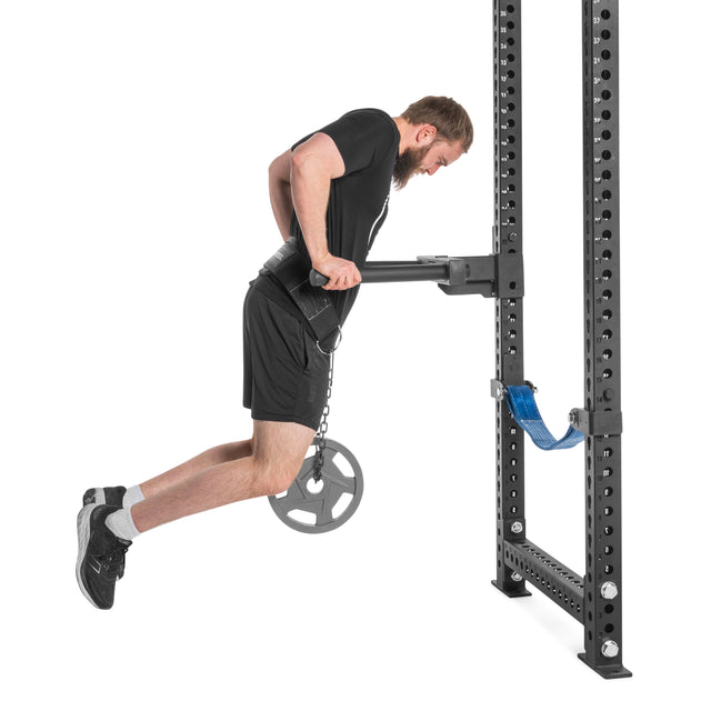 A man performs weighted dips on parallel bars attached to a power rack, using the Bells of Steel USA Dip Belt with reinforced stitching and a hanging weight plate, set against a plain white background.