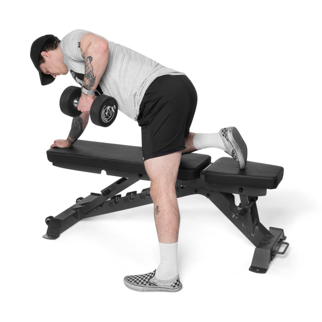 Wearing athletic gear, a person performs a single-arm dumbbell row with one knee and hand on the Buzz-Saw Heavy-Duty Adjustable Bench by Bells of Steel, while their other foot remains on the floor.