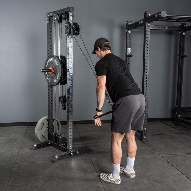 A man in a black shirt, gray shorts, and checkered shoes performs a cable triceps pushdown in the gym using the Bells of Steel USA Flat-Iron Tricep Press Cable Attachment for optimal tricep activation.