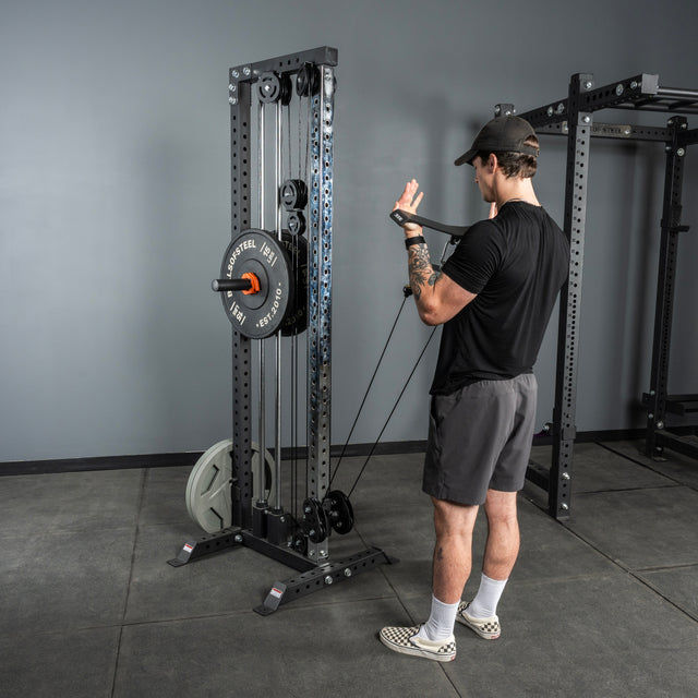 A person uses the Bells of Steel USA Flat-Iron Tricep Press Cable Attachment in a gym with gray walls and concrete floors, performing cable curls for optimal tricep activation while wearing a black shirt, gray shorts, and checkered shoes.