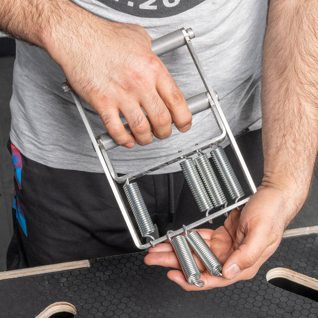 Someone inspects a Bells of Steel USA Adjustable Forearm Heavy Trainer, noting that one spring has come loose and appears to be repairing or examining the equipment.