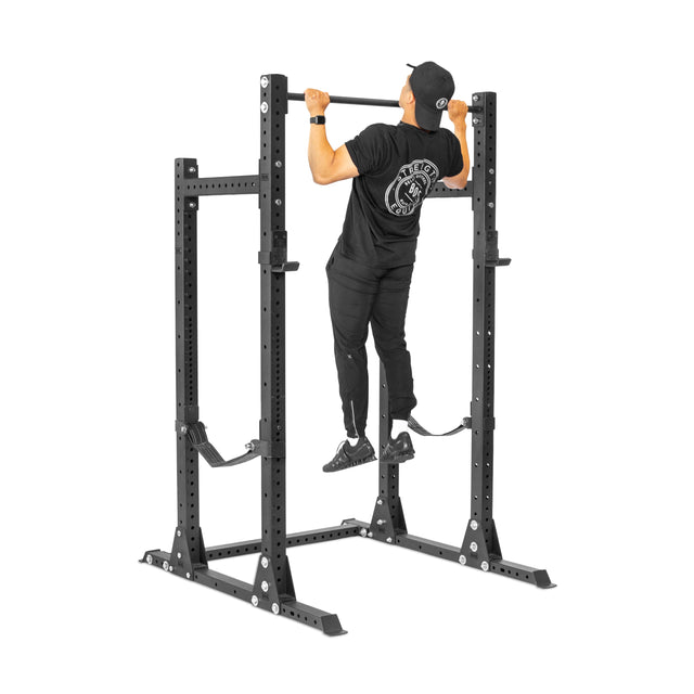 A person in black athletic wear performs a pull-up on the Bells of Steel Hydra Half Rack - Prebuilt (3" x 3", ⅝" Holes), a sturdy option with multiple adjustments—ideal for any home gym.