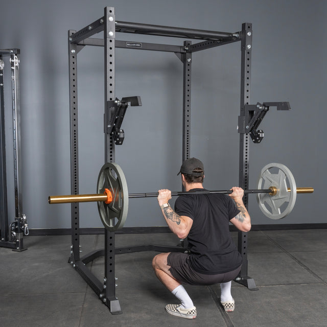 A man performs a squat inside a power rack using the Bells of Steel Monolift Rack Attachment, holding a loaded barbell across his shoulders. This space-saving gym equipment features an adjustable monolift for efficient lifting.