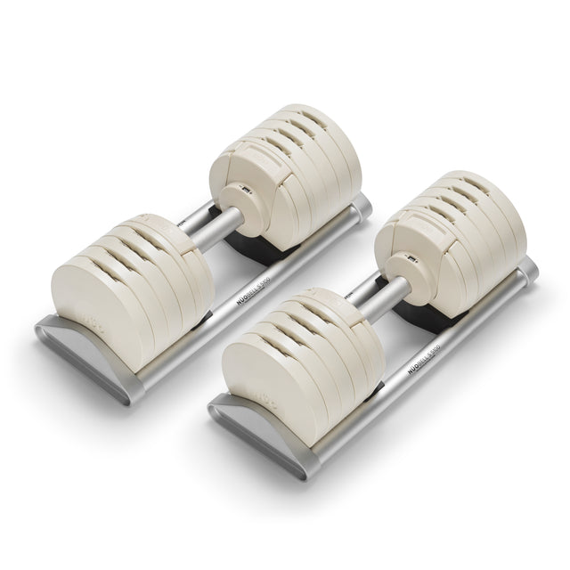 A pair of Bells of Steel USA NÜOBELL-S Adjustable Dumbbells with a sleek, modern design and metallic handles on silver stands—featuring multiple weight plates, they're ideal for any home gym.