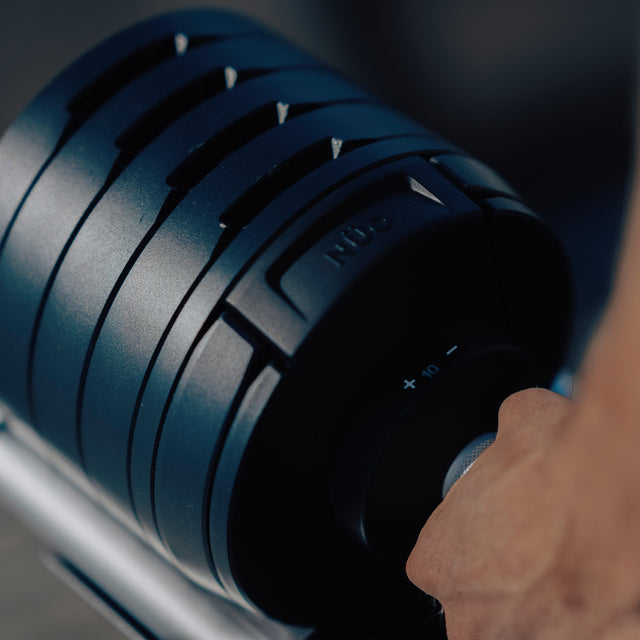 Close-up of a hand gripping the handle of the Bells of Steel USA NÜOBELL-S Adjustable Dumbbells, highlighting the weight selection dial and stacked plates—ideal for any home gym setup.