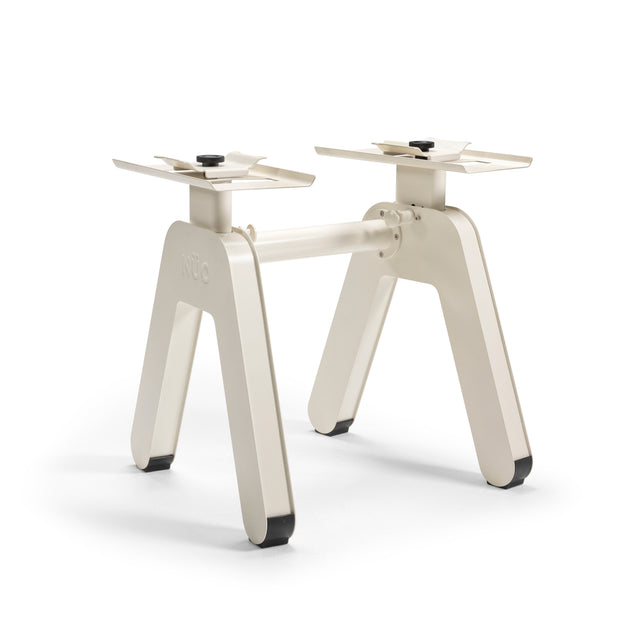 The NÜOBELL-S Floor Stand by Bells of Steel USA features a cream-colored metal base with two angled legs per side and a horizontal bar, offering a sleek, modern design ideal for use as an adjustable dumbbell or floor stand.
